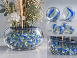 Conceptual CGI: Transparent small display vessel with decorative ribbon glass marbles used as a stable ornamental fill under a dry arrangement support; no food, no children or toys
