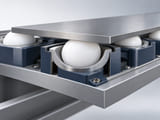 CGI conceptual: corte de un sistema de transferencia en transportador de baja carga con esfera blanca de UHMWPE retenida en una copa ancha bajo una pequeña pieza metálica plana; contacto de rodadura libre verosímil