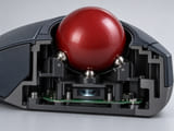 Konzeptionelle CGI-Darstellung: Schnitt durch ein industrielles Trackball-Modul mit großer roter, dezent strukturierter Harzkugel auf drei kleinen Stützkugeln, optischem Sensorfenster darunter und kompaktem schwarzem Gehäuse; plausible Geometrie